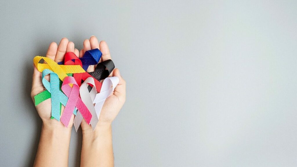 World cancer day (February 4). A pair of hands holding awareness ribbons; blue, red, green, black, grey, white, pink and yellow color for supporting people living and illness.