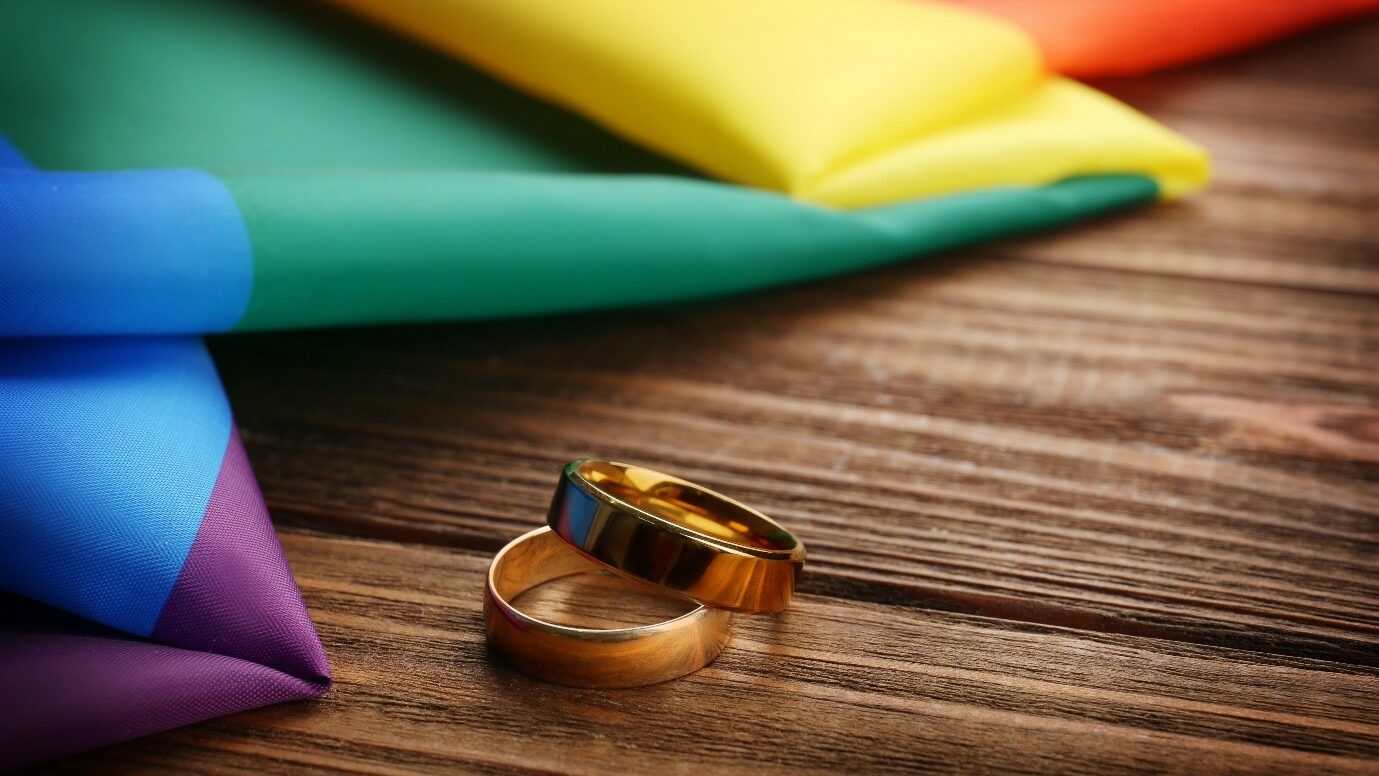 Two wedding rings and rainbow gay flag on wooden background.